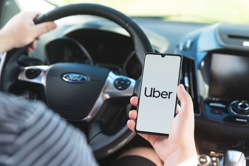 Uber driver holding smartphone in car. Uber is sharing-economy service for urban transport.