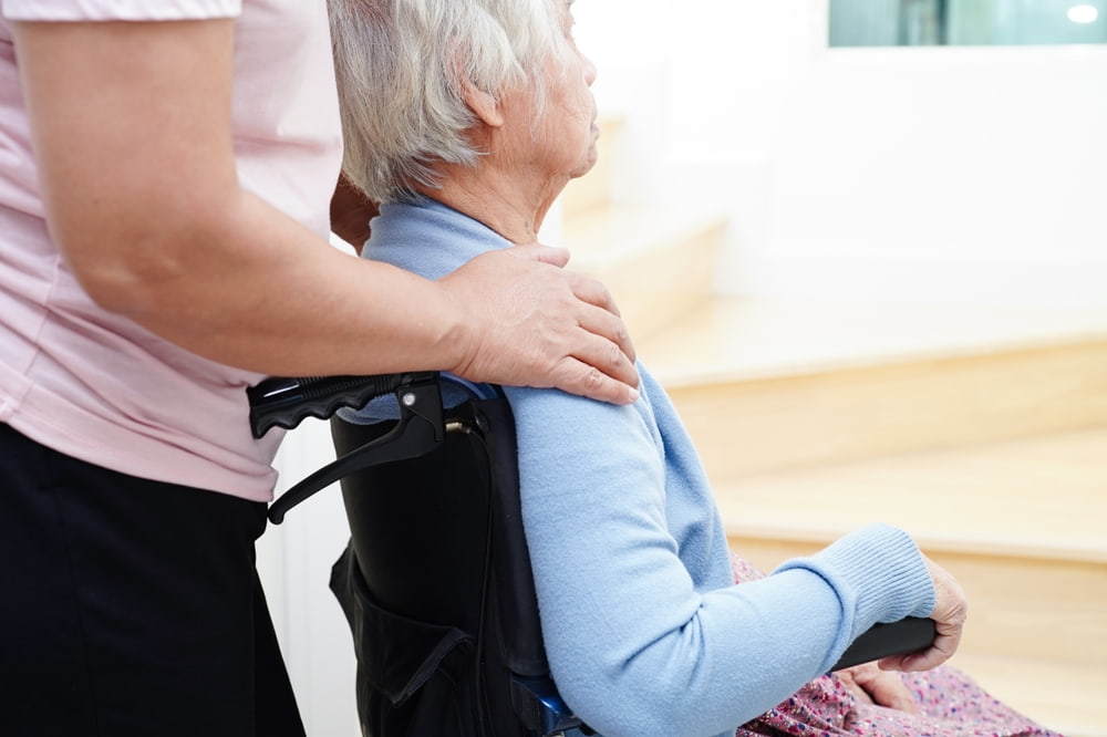 Caregiver resting a hand on the shoulder of an elderly woman in a wheelchair
