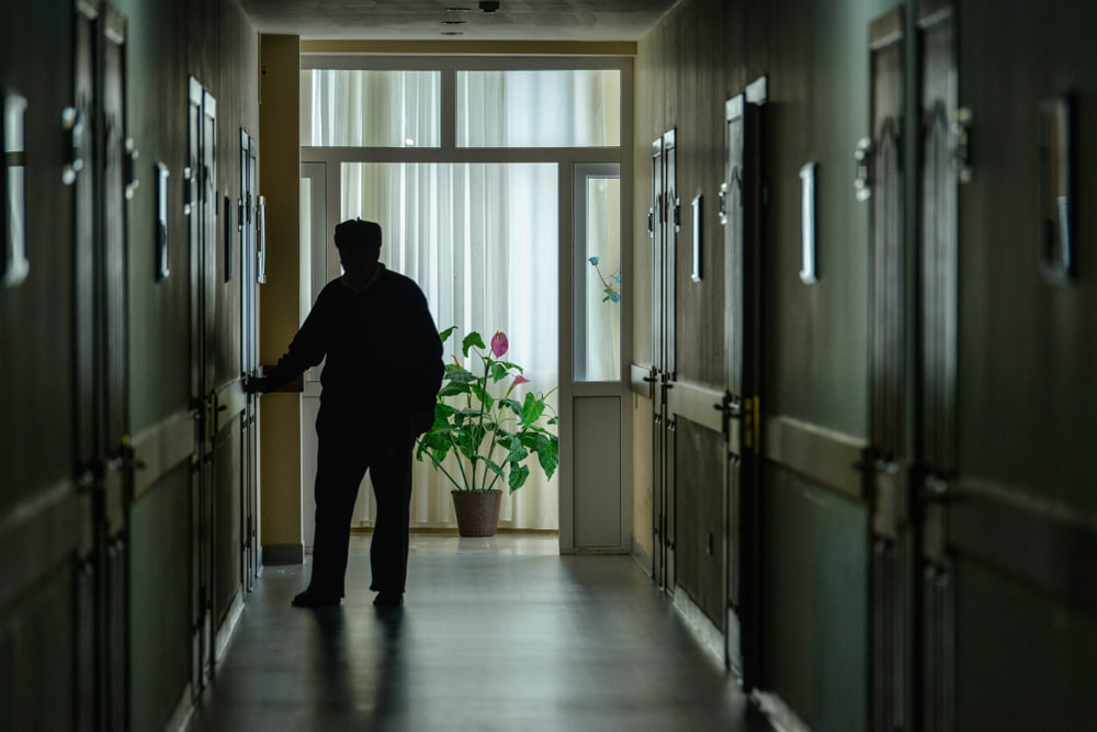 Silhouette of an elderly man walking through a dimly lit care facility corridor