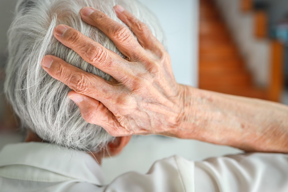 Elderly person holding the back of their head in pain