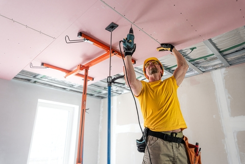 Construction worker drilling drywall on a ceiling overhead