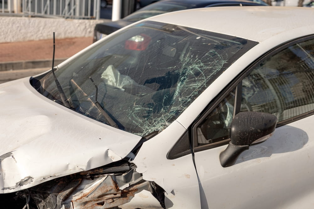 white car with a shattered windshield and front-end damage