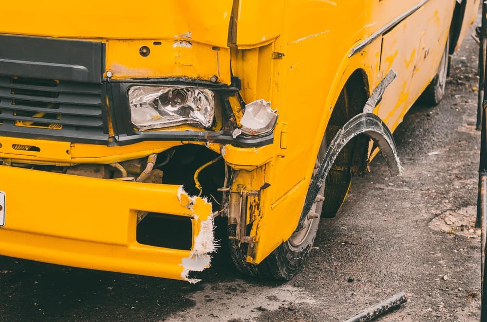 Close-up of extensive collision damage to the front corner of a yellow school bus

